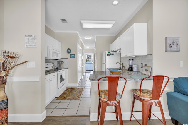 kitchen with white cabinetry, white appliances, a kitchen bar, and light tile patterned floors