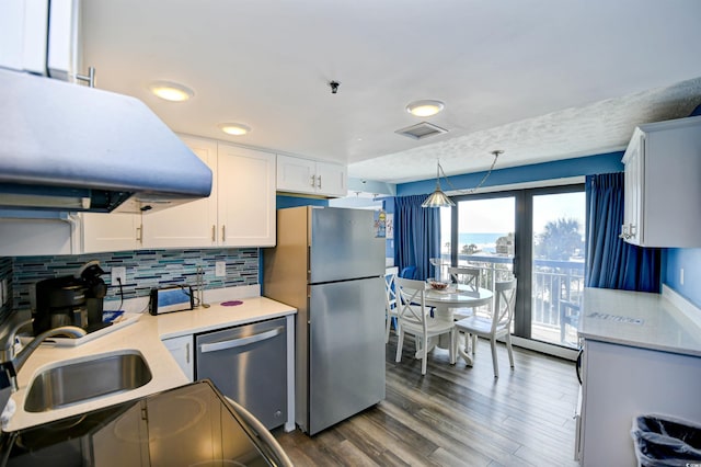 kitchen featuring dark wood-type flooring, appliances with stainless steel finishes, white cabinetry, hanging light fixtures, and tasteful backsplash