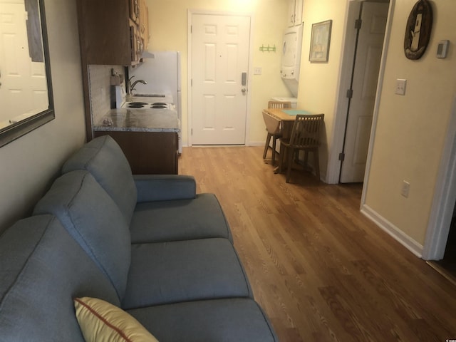 living room featuring hardwood / wood-style flooring, stacked washer / drying machine, and sink