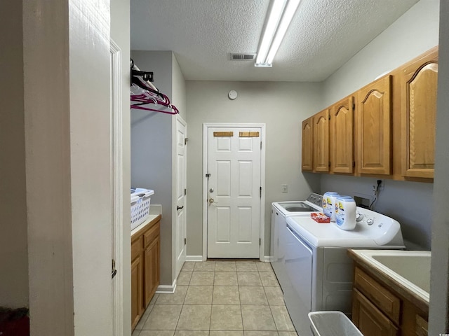 laundry area with light tile patterned flooring, sink, cabinets, washing machine and dryer, and a textured ceiling