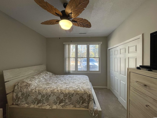 carpeted bedroom with ceiling fan, a closet, and a textured ceiling