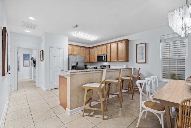 kitchen with a breakfast bar, stainless steel appliances, light stone counters, light tile patterned flooring, and kitchen peninsula