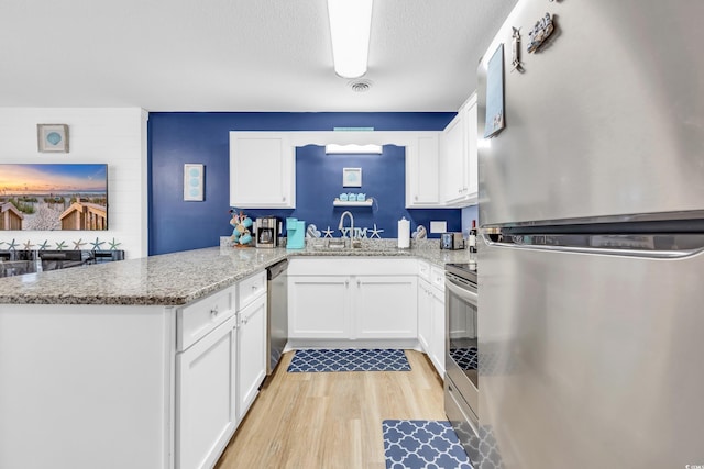 kitchen with a peninsula, a sink, light wood-style floors, appliances with stainless steel finishes, and white cabinetry