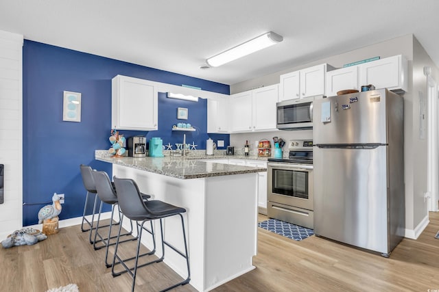 kitchen with a peninsula, appliances with stainless steel finishes, white cabinetry, light wood-type flooring, and a kitchen bar