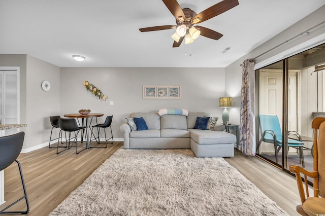 living room with light wood-style flooring, baseboards, visible vents, and ceiling fan