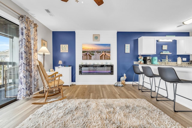 interior space featuring visible vents, a large fireplace, baseboards, ceiling fan, and light wood-style flooring