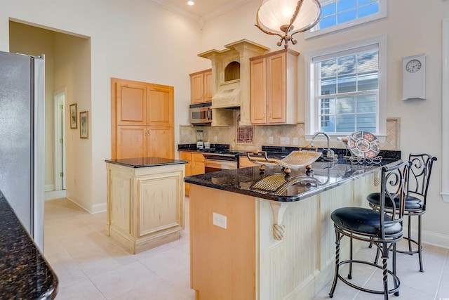 kitchen with dark stone countertops, light brown cabinets, appliances with stainless steel finishes, a kitchen island, and decorative backsplash