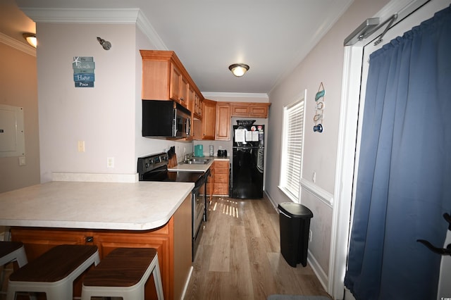 kitchen featuring ornamental molding, a kitchen breakfast bar, kitchen peninsula, light hardwood / wood-style floors, and black appliances