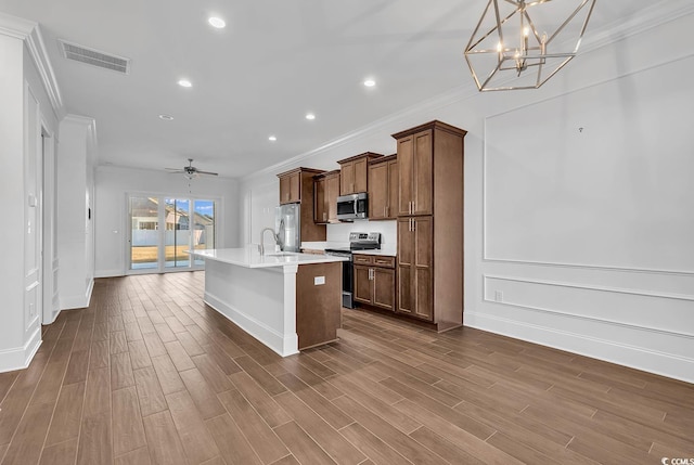 kitchen featuring ornamental molding, appliances with stainless steel finishes, a kitchen island with sink, hardwood / wood-style flooring, and ceiling fan with notable chandelier