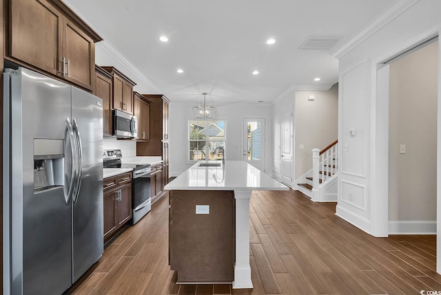 kitchen with a kitchen island with sink, crown molding, stainless steel appliances, and dark hardwood / wood-style floors