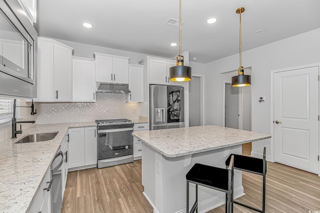 kitchen featuring stainless steel appliances, white cabinetry, a kitchen island, and decorative light fixtures