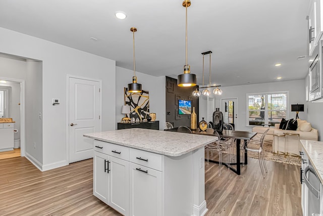 kitchen with decorative light fixtures, white cabinets, a center island, light stone counters, and light hardwood / wood-style flooring