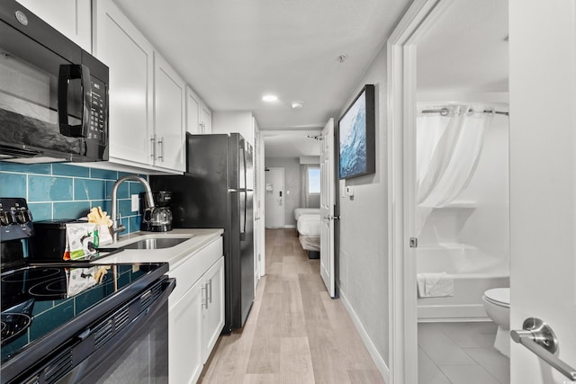 kitchen with sink, black appliances, light hardwood / wood-style floors, decorative backsplash, and white cabinets