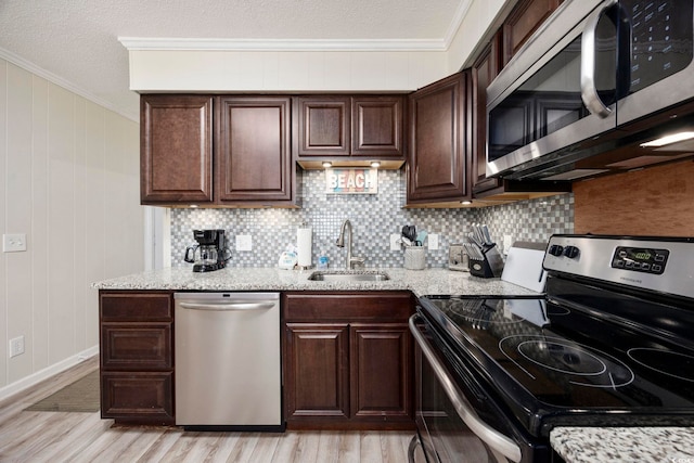 kitchen with appliances with stainless steel finishes, sink, ornamental molding, dark brown cabinetry, and light stone countertops