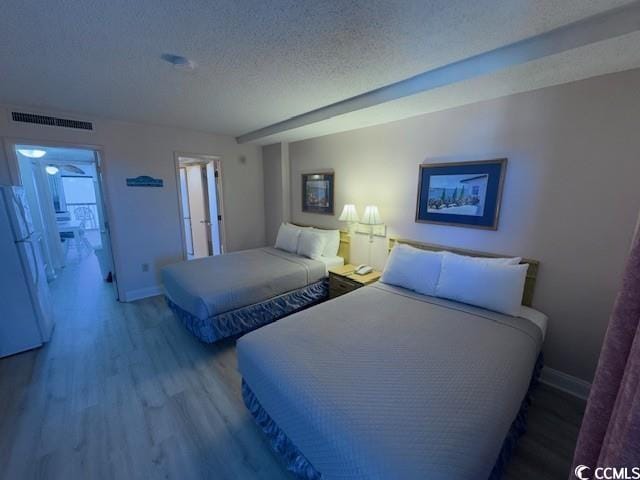 bedroom with white fridge, a textured ceiling, and light wood-type flooring