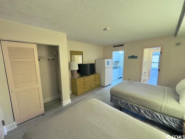 bedroom featuring white fridge, a textured ceiling, light hardwood / wood-style floors, and a closet