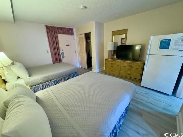 bedroom with white fridge, light hardwood / wood-style flooring, and a closet