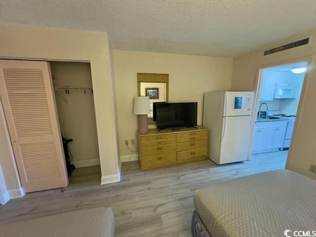 bedroom featuring sink, light wood-type flooring, a textured ceiling, and white refrigerator