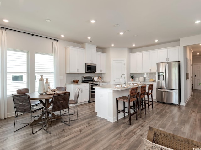 kitchen with sink, white cabinetry, appliances with stainless steel finishes, a kitchen breakfast bar, and a kitchen island with sink