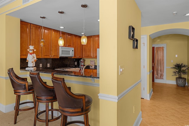 kitchen featuring pendant lighting, a kitchen breakfast bar, kitchen peninsula, and dark stone counters