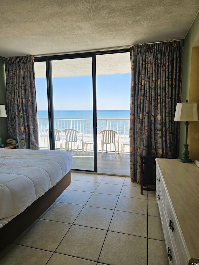 tiled bedroom with a water view, access to outside, a textured ceiling, and a wall of windows