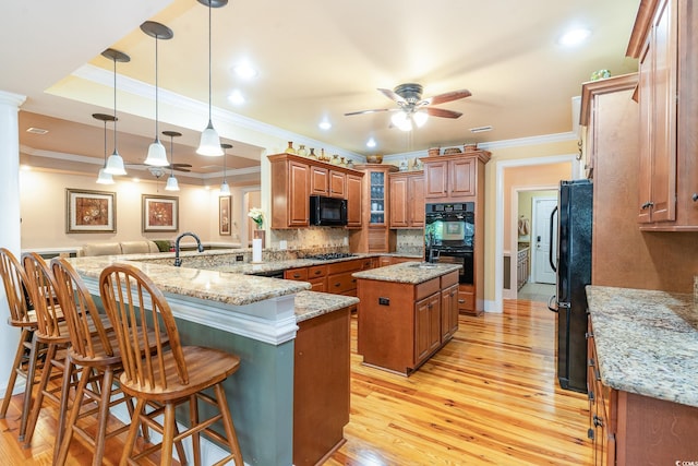 kitchen featuring a kitchen island, a breakfast bar, kitchen peninsula, light stone counters, and black appliances