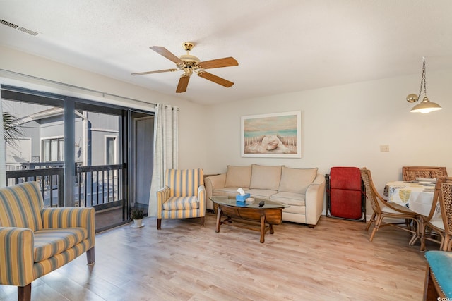 living room featuring ceiling fan, light hardwood / wood-style flooring, and a textured ceiling