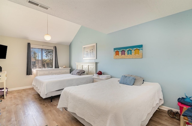 bedroom with lofted ceiling, light hardwood / wood-style floors, and a textured ceiling