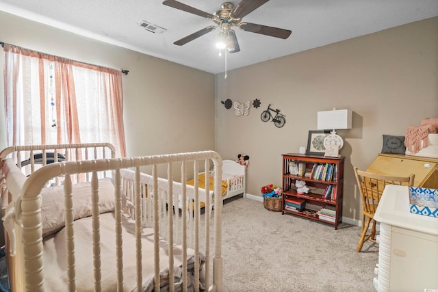 carpeted bedroom with ceiling fan and a crib