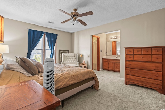 bedroom featuring ensuite bath, sink, light colored carpet, ceiling fan, and a textured ceiling