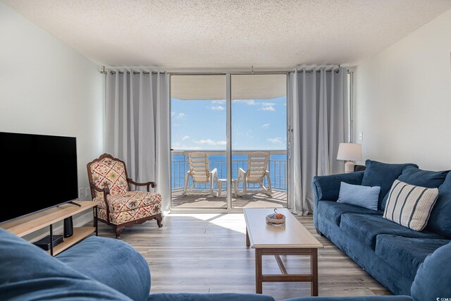 living room with floor to ceiling windows, a water view, hardwood / wood-style floors, and a textured ceiling