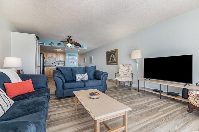 living room featuring ceiling fan, sink, a textured ceiling, and light hardwood / wood-style flooring