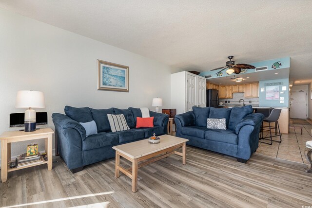 living room featuring ceiling fan, sink, light hardwood / wood-style flooring, and a textured ceiling