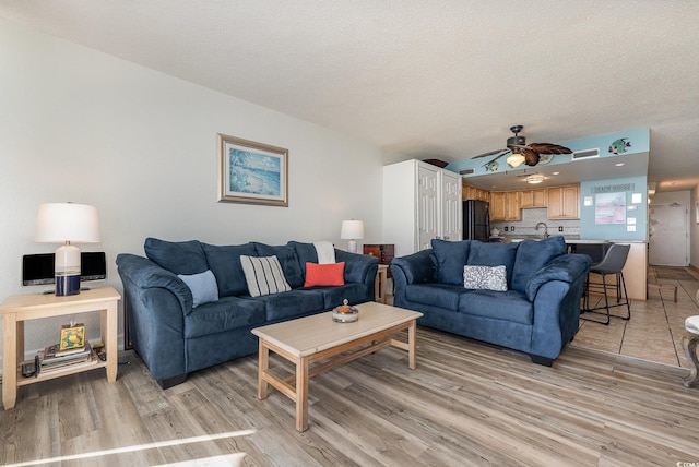 living area with visible vents, ceiling fan, a textured ceiling, and light wood finished floors