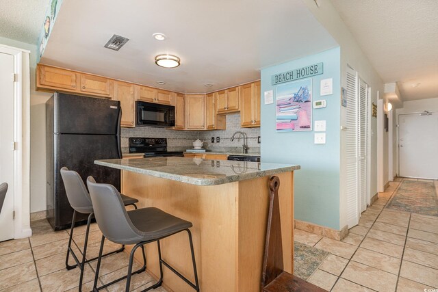 kitchen featuring light tile patterned floors, a breakfast bar area, backsplash, a center island, and black appliances