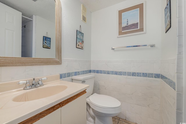 full bath featuring a textured ceiling, toilet, visible vents, vanity, and tile walls