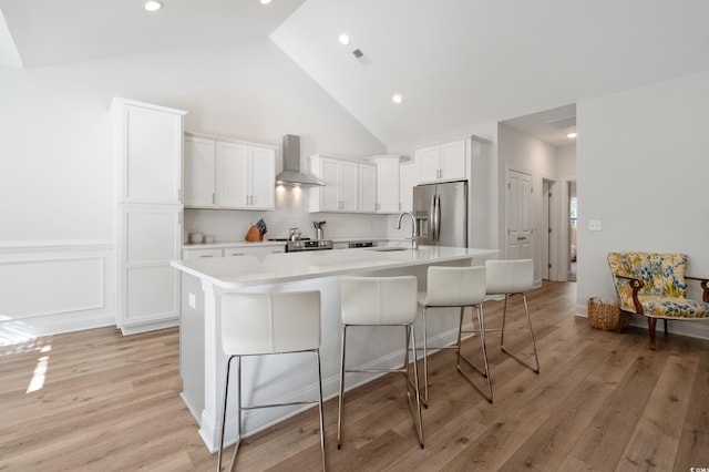 kitchen with appliances with stainless steel finishes, white cabinetry, sink, a kitchen bar, and wall chimney exhaust hood