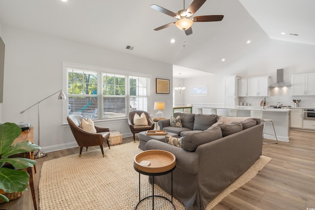 living room with high vaulted ceiling, ceiling fan with notable chandelier, and light wood-type flooring