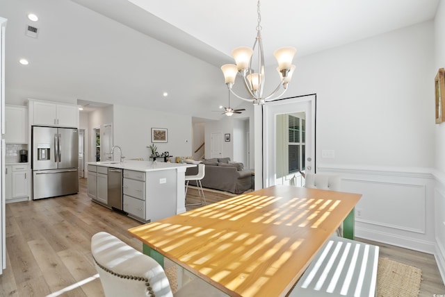 dining area with ceiling fan with notable chandelier, vaulted ceiling, sink, and light wood-type flooring