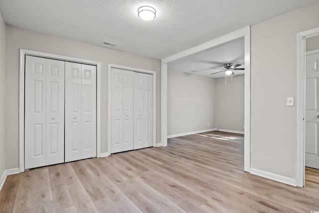 unfurnished bedroom featuring ceiling fan, two closets, light hardwood / wood-style floors, and a textured ceiling