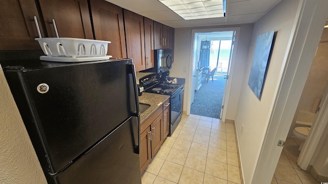 kitchen with stone counters, light tile patterned flooring, a drop ceiling, and black appliances