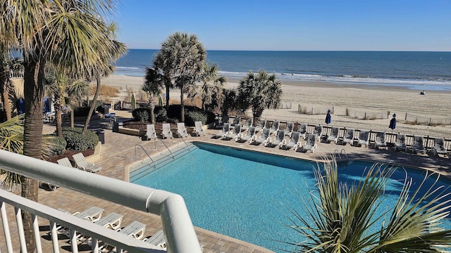 view of swimming pool with a water view, a beach view, and a patio area