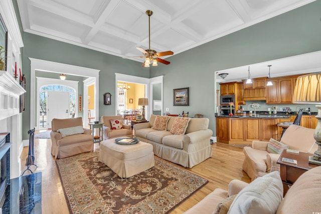 living room featuring coffered ceiling, light wood-type flooring, beamed ceiling, ceiling fan with notable chandelier, and a high ceiling