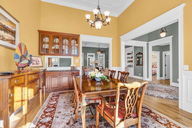 dining room with ceiling fan with notable chandelier, ornamental molding, and light hardwood / wood-style floors