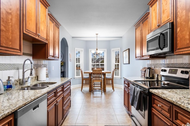 kitchen with light tile patterned flooring, sink, appliances with stainless steel finishes, pendant lighting, and light stone countertops