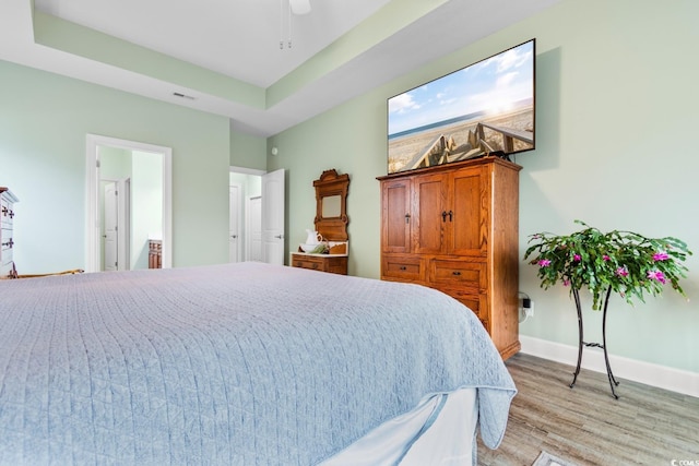 bedroom with ceiling fan, a tray ceiling, and light hardwood / wood-style flooring