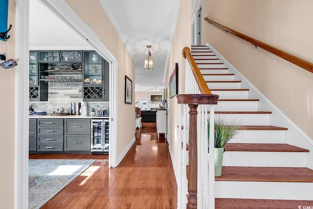 stairs with hardwood / wood-style flooring, ornamental molding, bar area, and beverage cooler