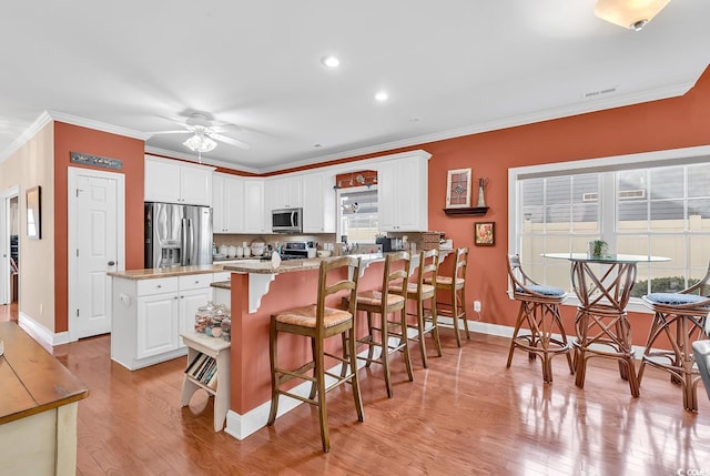 kitchen with light stone counters, stainless steel appliances, a kitchen bar, and white cabinets