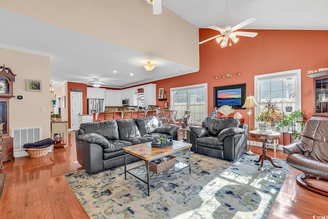 living room with ornamental molding, high vaulted ceiling, ceiling fan, and light wood-type flooring