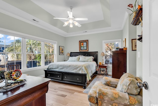 bedroom with ornamental molding, light hardwood / wood-style flooring, ceiling fan, and a tray ceiling